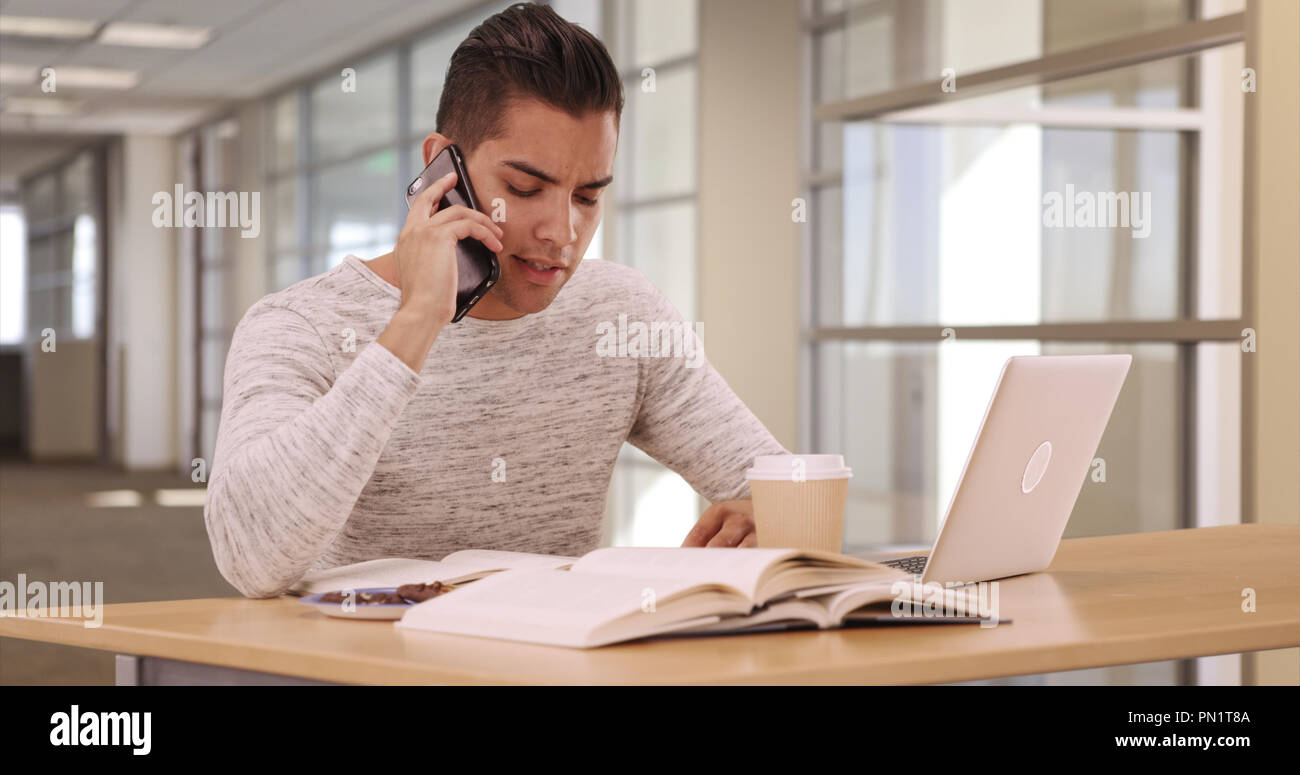 Des étudiants de l'université Latino millénaire dans la bibliothèque du campus avec ordinateur portable et téléphone portable Banque D'Images