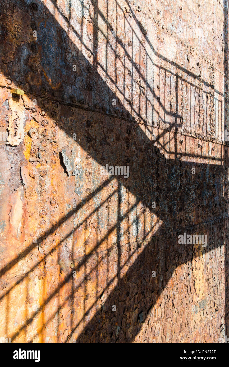 Panneaux en acier rouillé sur un vieux navire, fissurés et texturé avec peinture écaillée et Rusty rivets. Les ombres d'escalier métallique sur la surface en fonte Banque D'Images
