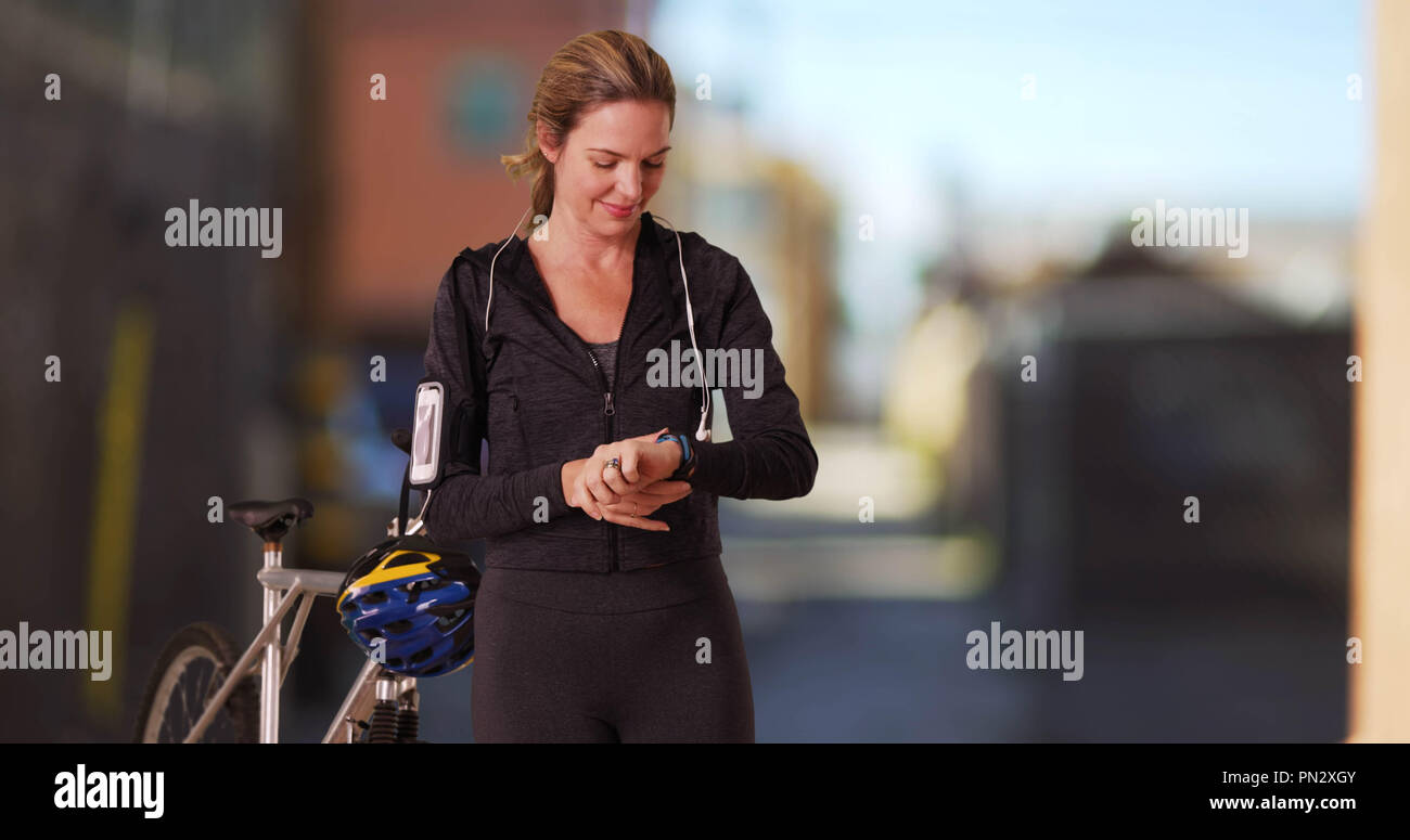 Caucasian woman in athletic wear l'utilisation de device post entraînement avec vélo en alley Banque D'Images