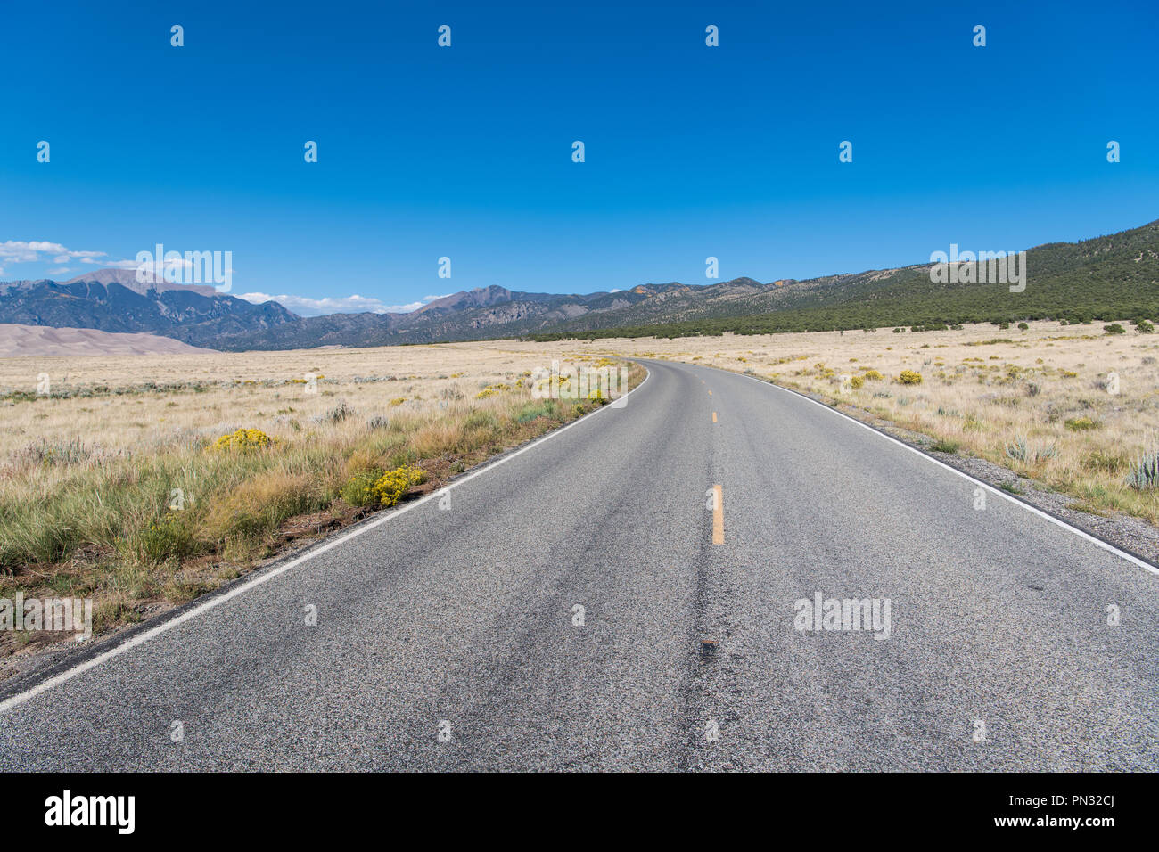 Courbe de l'autoroute à la perspective avec les plaines herbeuses sous un ciel bleu parfait vers les montagnes Rocheuses, à Great Sand Dunes National Park Banque D'Images