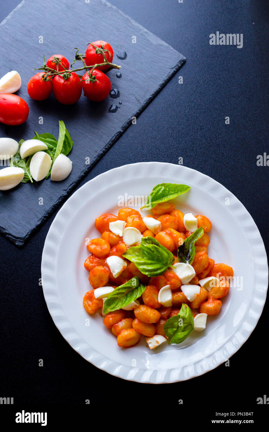 Alla Sorrentina gnocchi de pommes de terre à la sauce tomate avec du basilic vert et boules de mozzarella servi sur une assiette et les ingrédients sur conseil de schiste noir sur b Banque D'Images