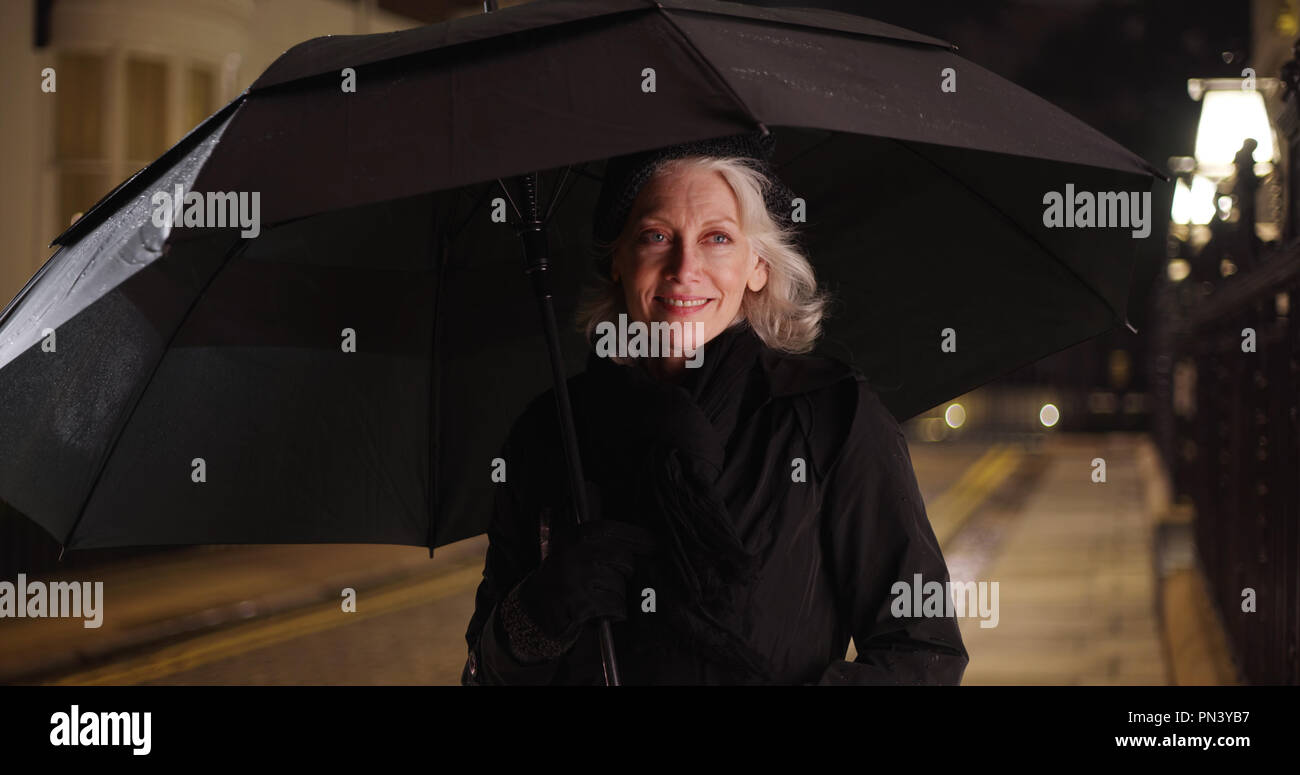 Happy woman standing under umbrella on nuit pluvieuse dans la ville Banque D'Images