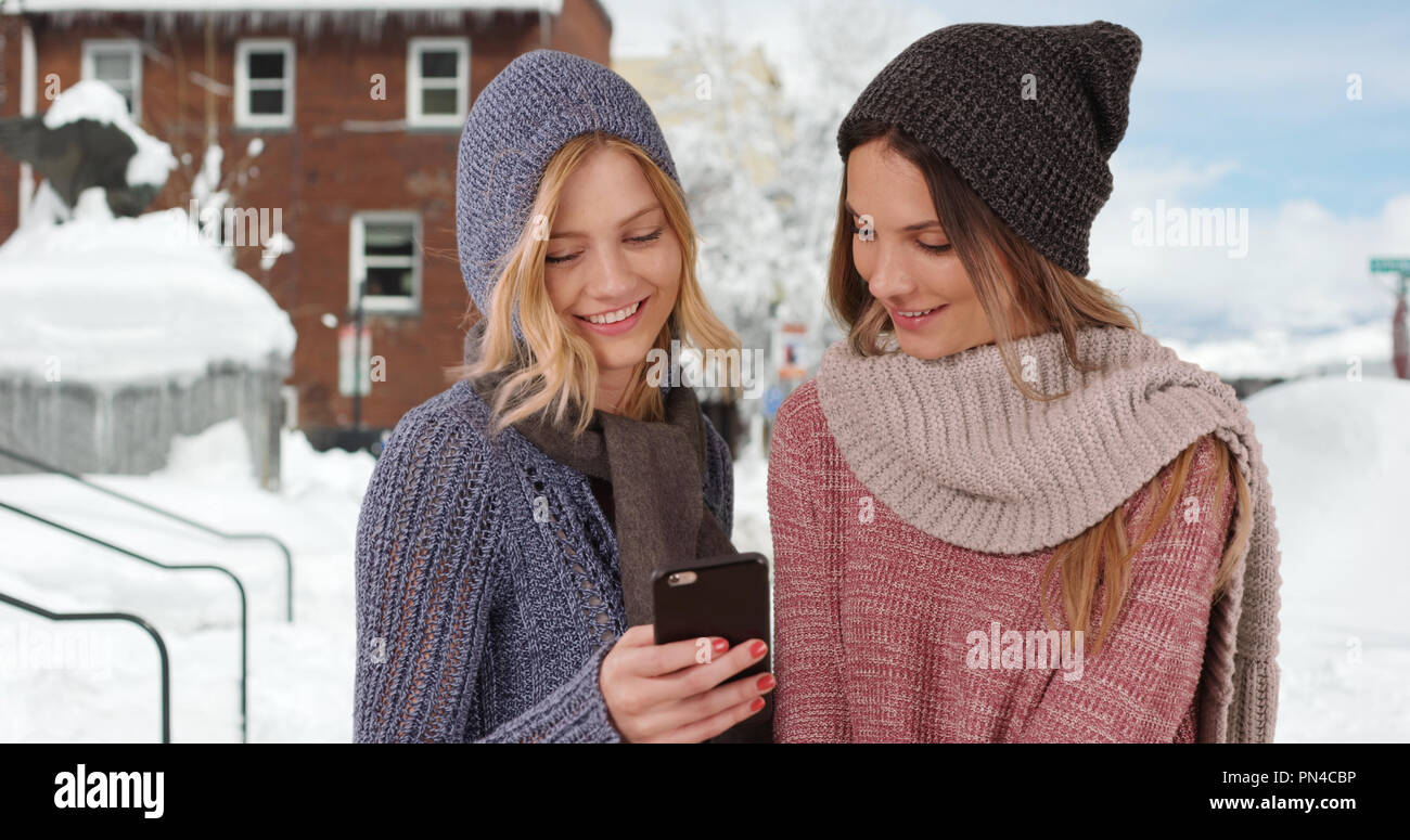 Deux jeunes filles habillé pour l'hiver à l'aide de l'extérieur du smartphone dans quartier enneigé Banque D'Images