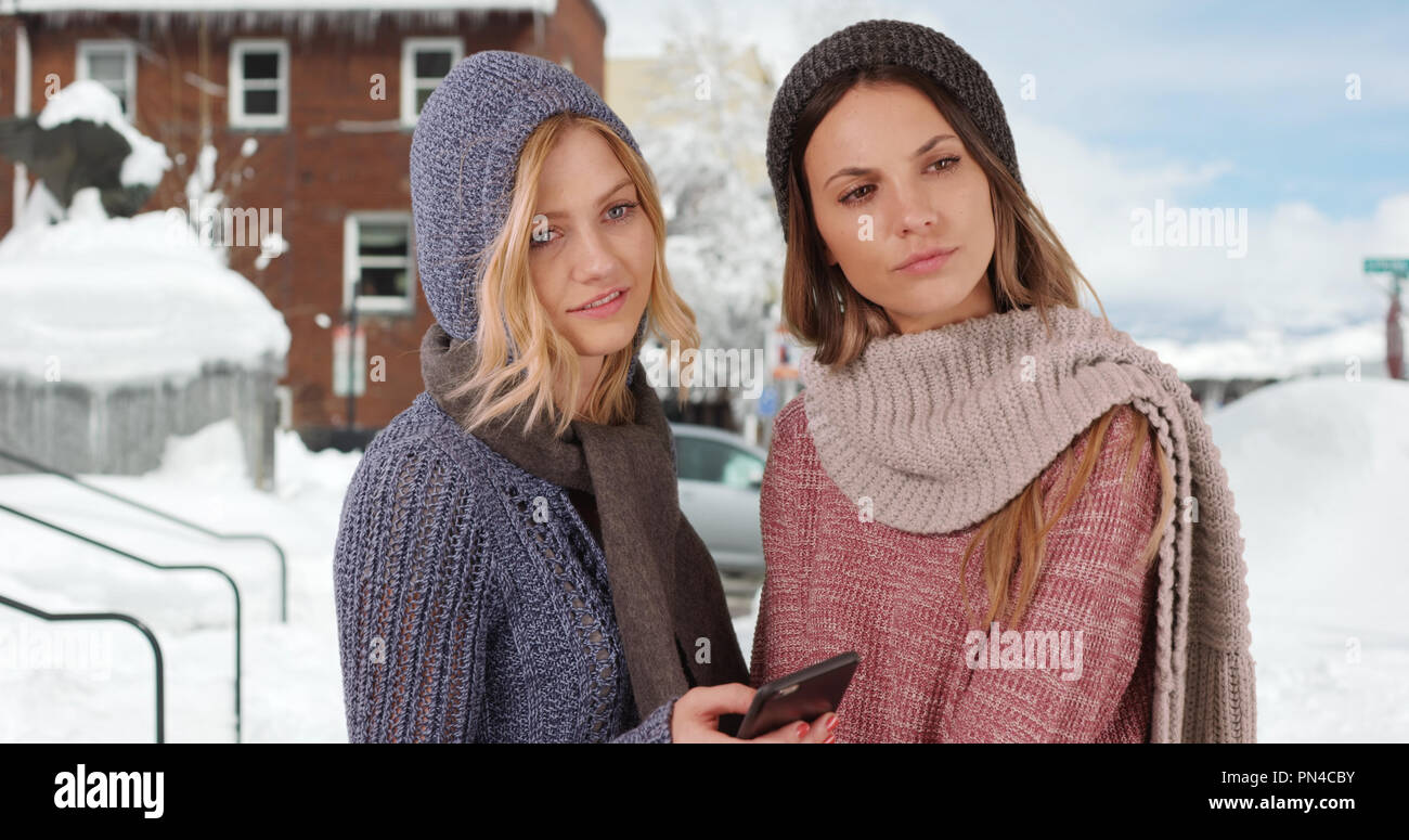 Deux jeunes filles habillé pour l'hiver à l'aide de l'extérieur du smartphone dans quartier enneigé Banque D'Images
