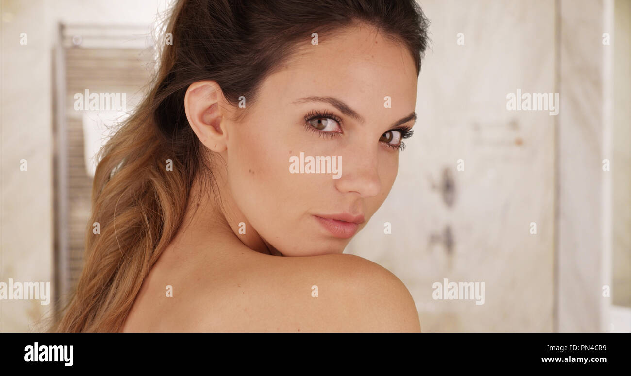 Jeune modèle attrayant à la recherche sur l'épaule et se faisant passer pour l'appareil photo dans la salle de bains Banque D'Images