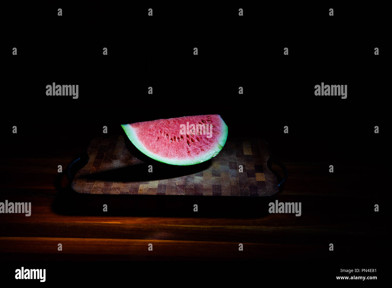 Grande tranche de pastèque sur planche à découper sur fond sombre sous spot light Banque D'Images