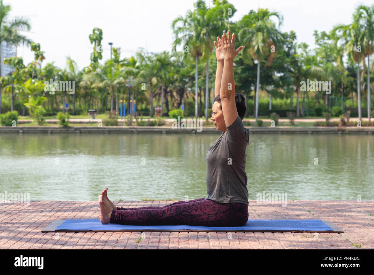 Femme asiatique sains d'âge moyen assis et lever les bras pour lancer paschimottanasana yoga pose au parc de la ville à la vie saine. matin et concept Banque D'Images