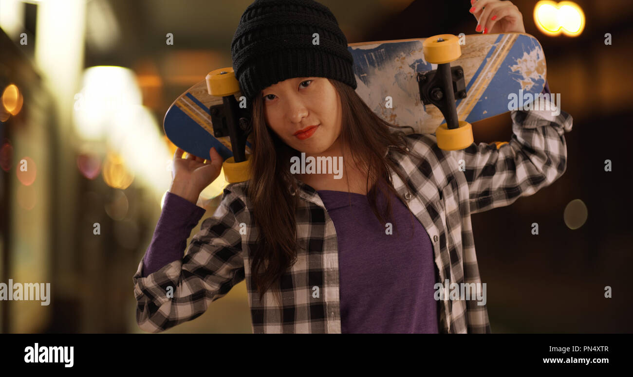 Fermer la vue de woman holding skateboard sur les épaules en quartier urbain Banque D'Images