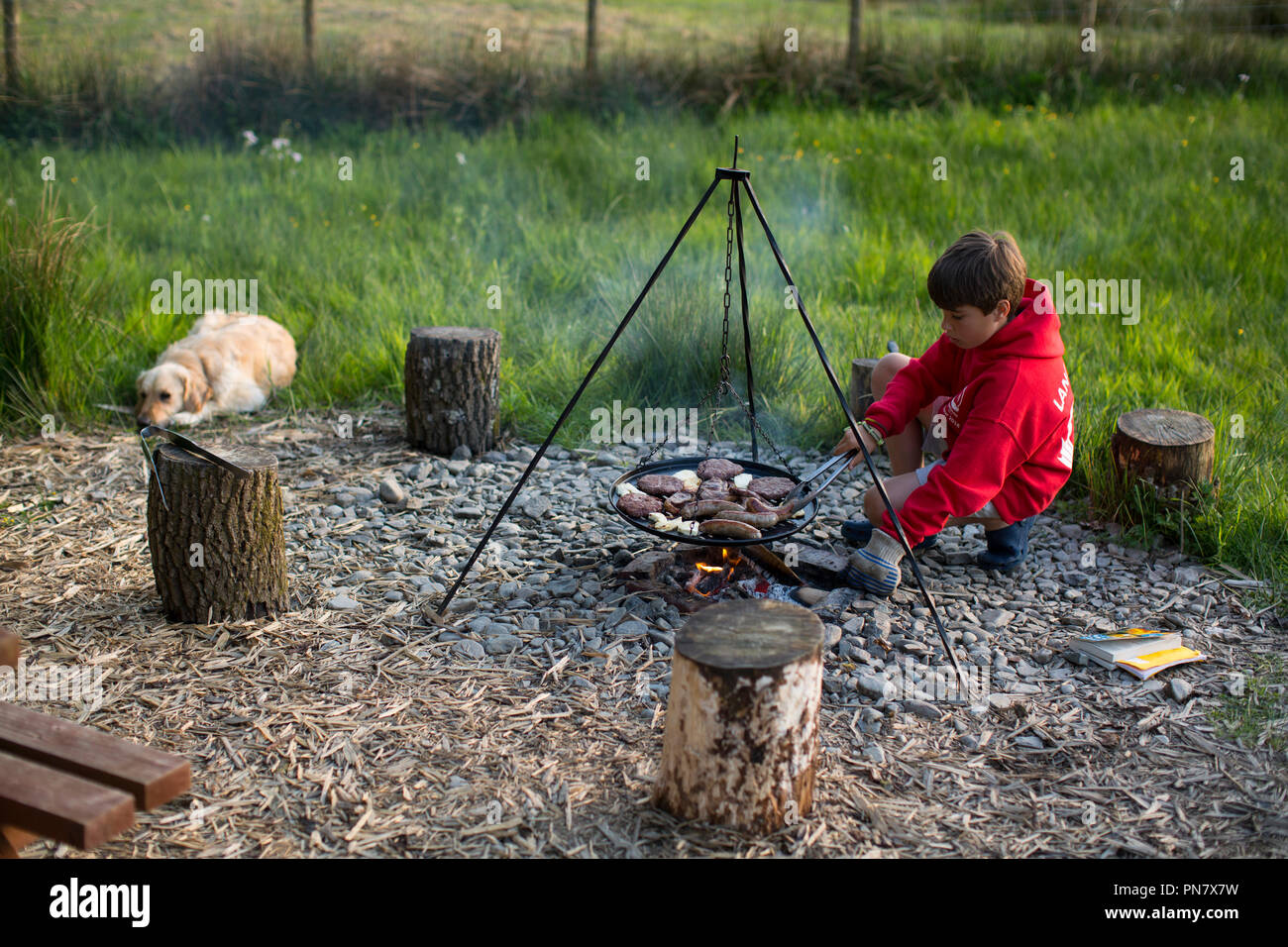 Un jeune garçon à la cuisson sur un feu de camp. Banque D'Images