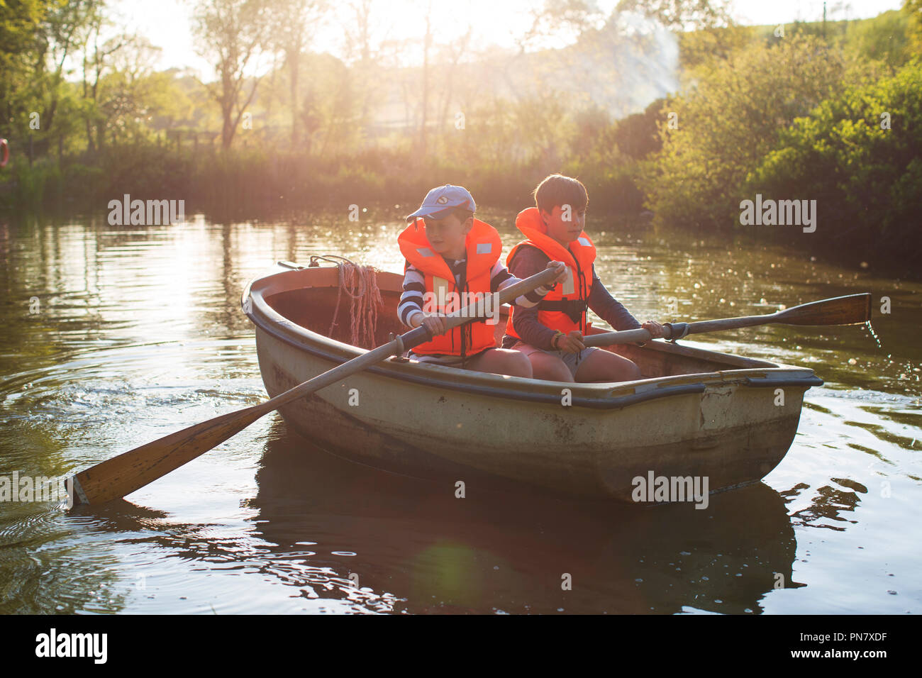 Deux garçons rowinig un bateau sur un petit lac retour éclairé par le soleil du soir. Banque D'Images