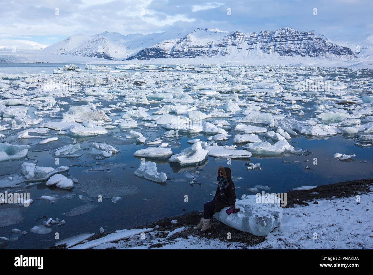Touriste est assis sur un bloc de glace à Jokulsarlon glacial Lagoon, parc national du Vatnajökull, au Sud Est de l'Islande Banque D'Images