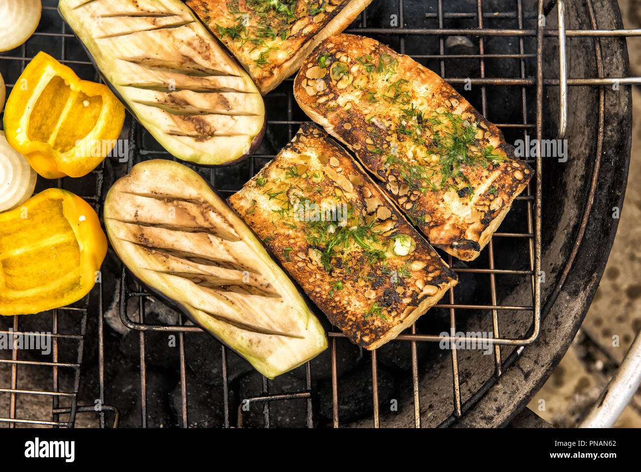 Close up of pain à l'ail chaud et assortiment d'aubergines grillées, oignons et poivrons sur la grille en métal de grand ronde grill extérieur. Focus sélectif. Banque D'Images