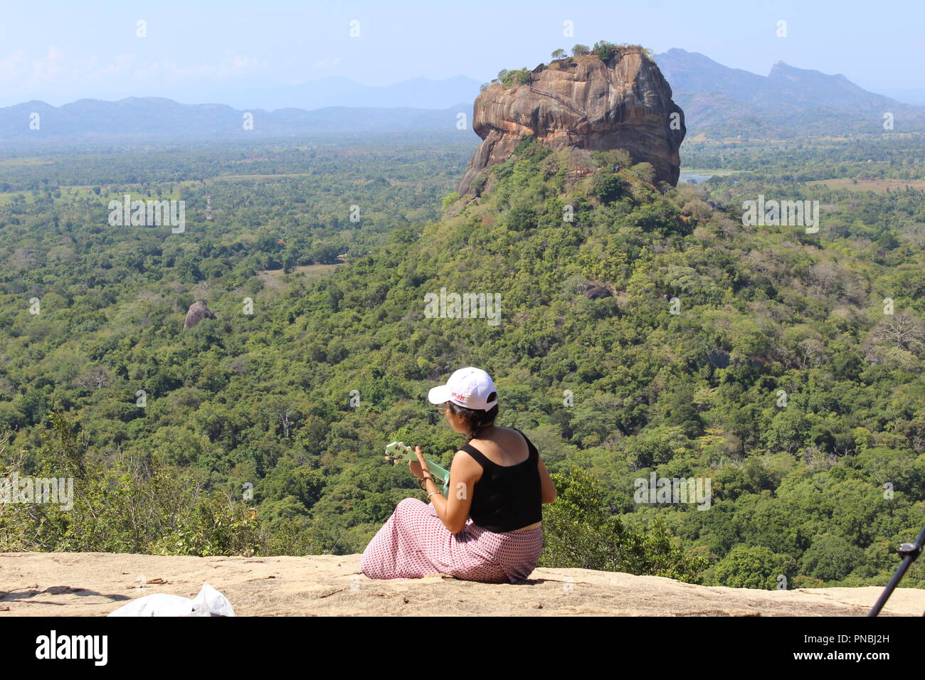 Asian girl à jouer de la guitare en haut de Pidurangala Rock devant le rocher du lion Sigiriya, Sri Lanka Banque D'Images