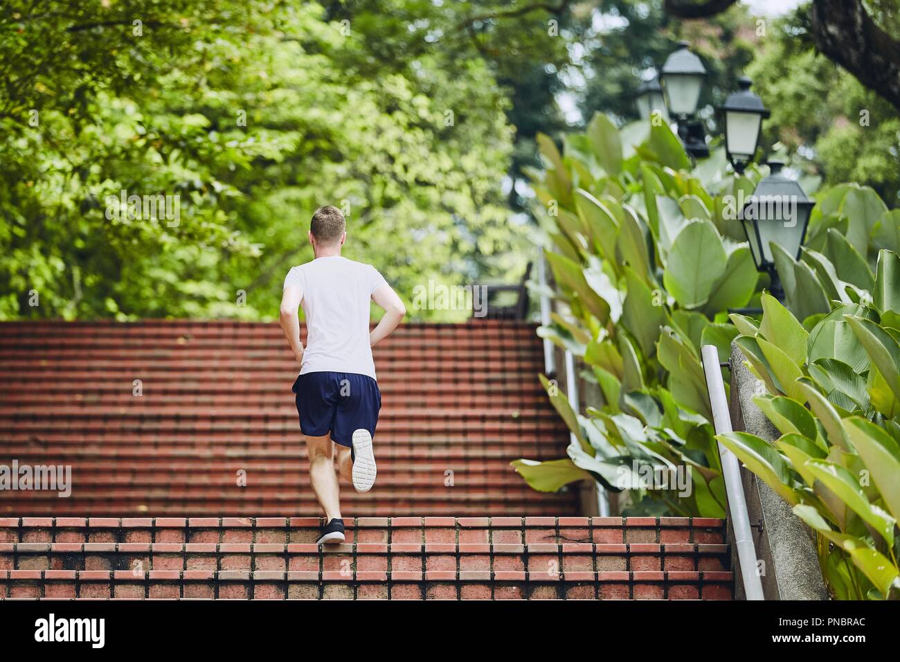 Sport dans la ville. Jeune homme courir vers le haut escalier extérieur en parc public. Banque D'Images