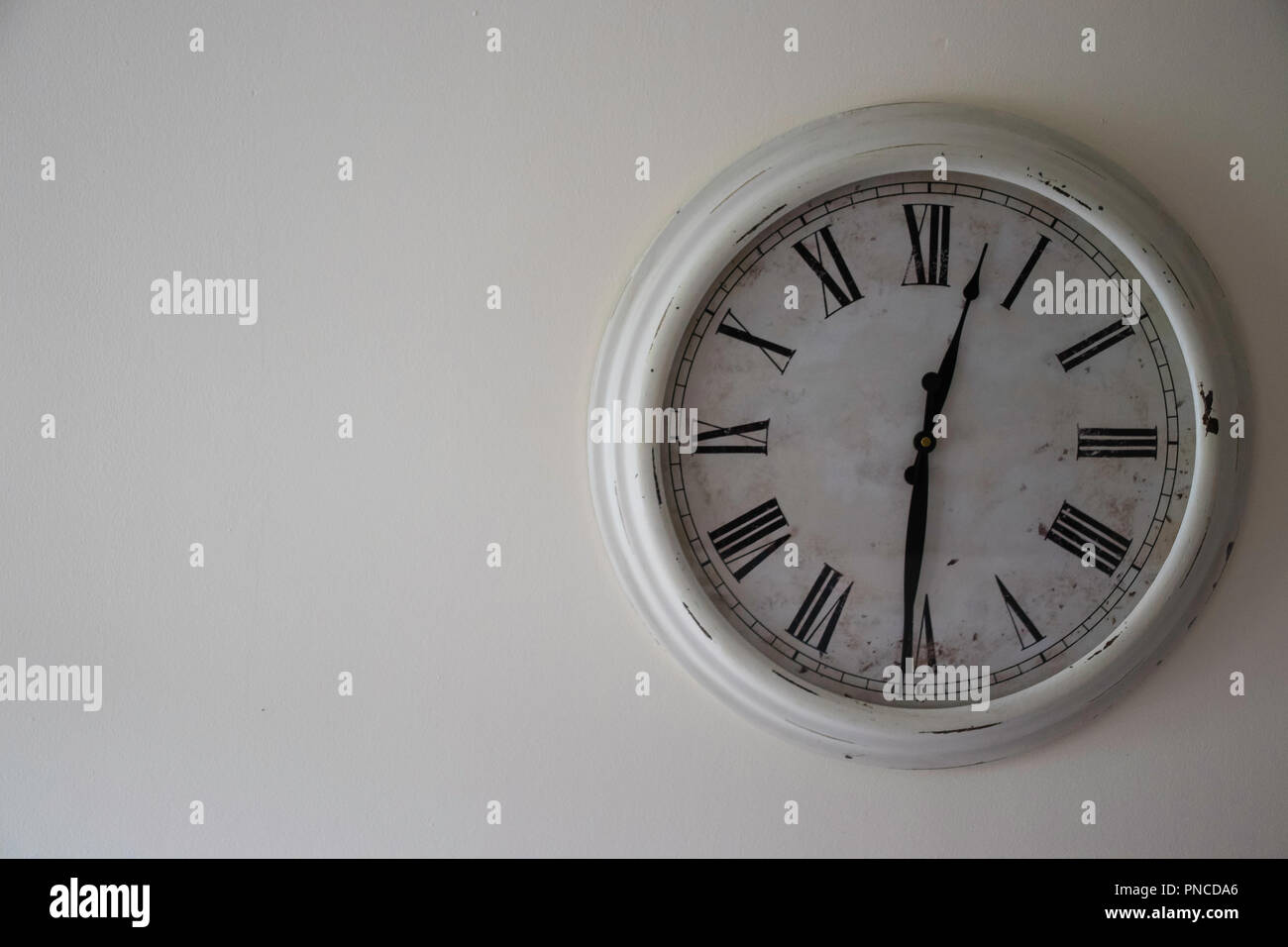Horloge vintage blanche sur un mur crème réglé sur l'heure du déjeuner (12h30) Banque D'Images