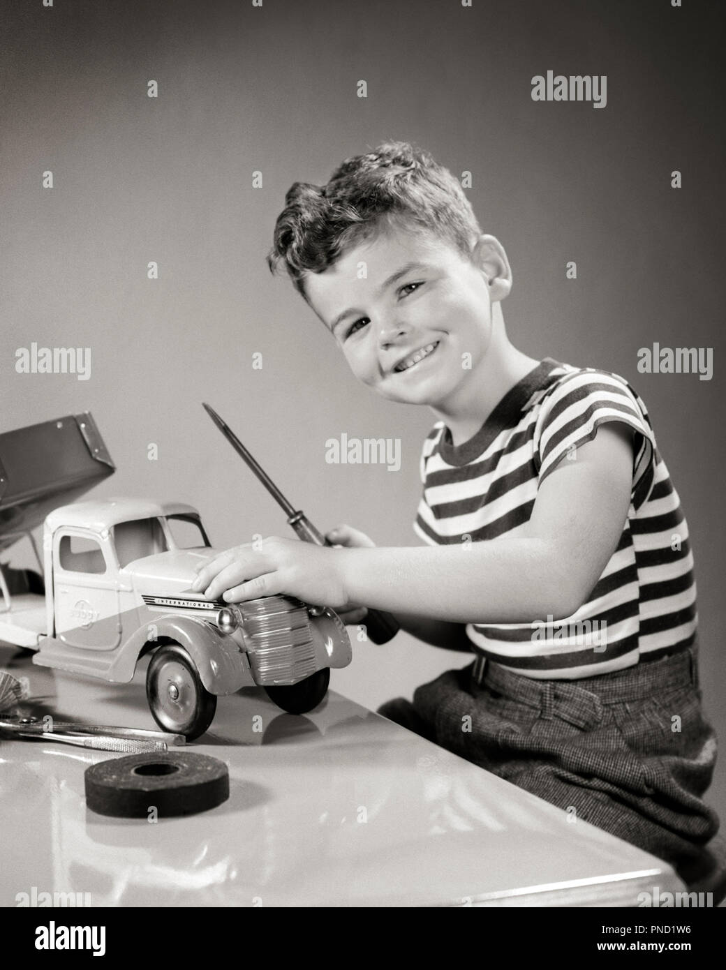 1940 SMILING BOY LOOKING AT CAMERA PLAYING WITH TOY TRUCK EFFECTUER LES RÉPARATIONS AVEC TOURNEVIS - j10555 HAR001 RÉPARATIONS HARS SMILES FRIENDLY TOURNEVIS JOYEUX MINEURS NOIR ET BLANC DE L'ORIGINE ETHNIQUE CAUCASIENNE HAR001 old fashioned Banque D'Images