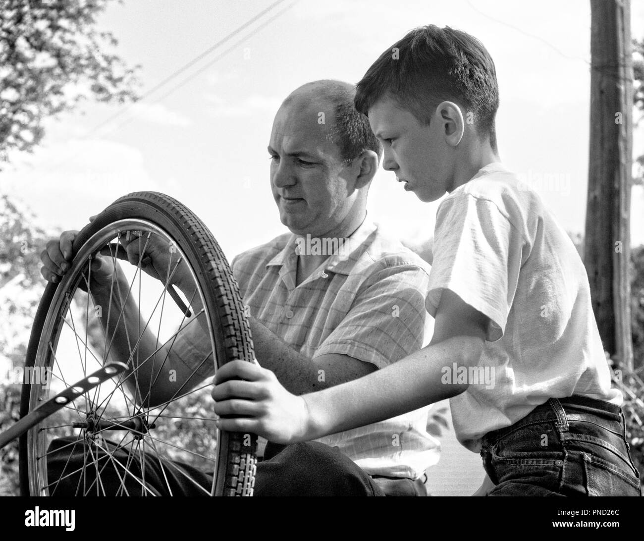 Années 1950 Années 1960 PÈRE ET FILS FIXANT LE PNEU SUR LA LOCATION - j4518 HAR001 HARS, mi-longueur de la vie de personnes qui s'OCCUPENT DE LA CONFIANCE DES HOMMES PÈRES DE FIXATION B&W ET LES PAPAS AUTORITÉ CONNAISSANCES CROISSANCE RÉPARATION mineurs adultes mi-homme mi-adulte l'unité NOIR ET BLANC DE L'ORIGINE ETHNIQUE CAUCASIENNE HAR001 old fashioned Banque D'Images