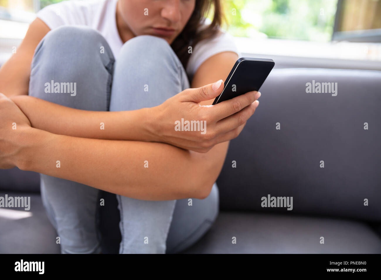 Young Woman Sitting on Sofa Using Smartphone Banque D'Images