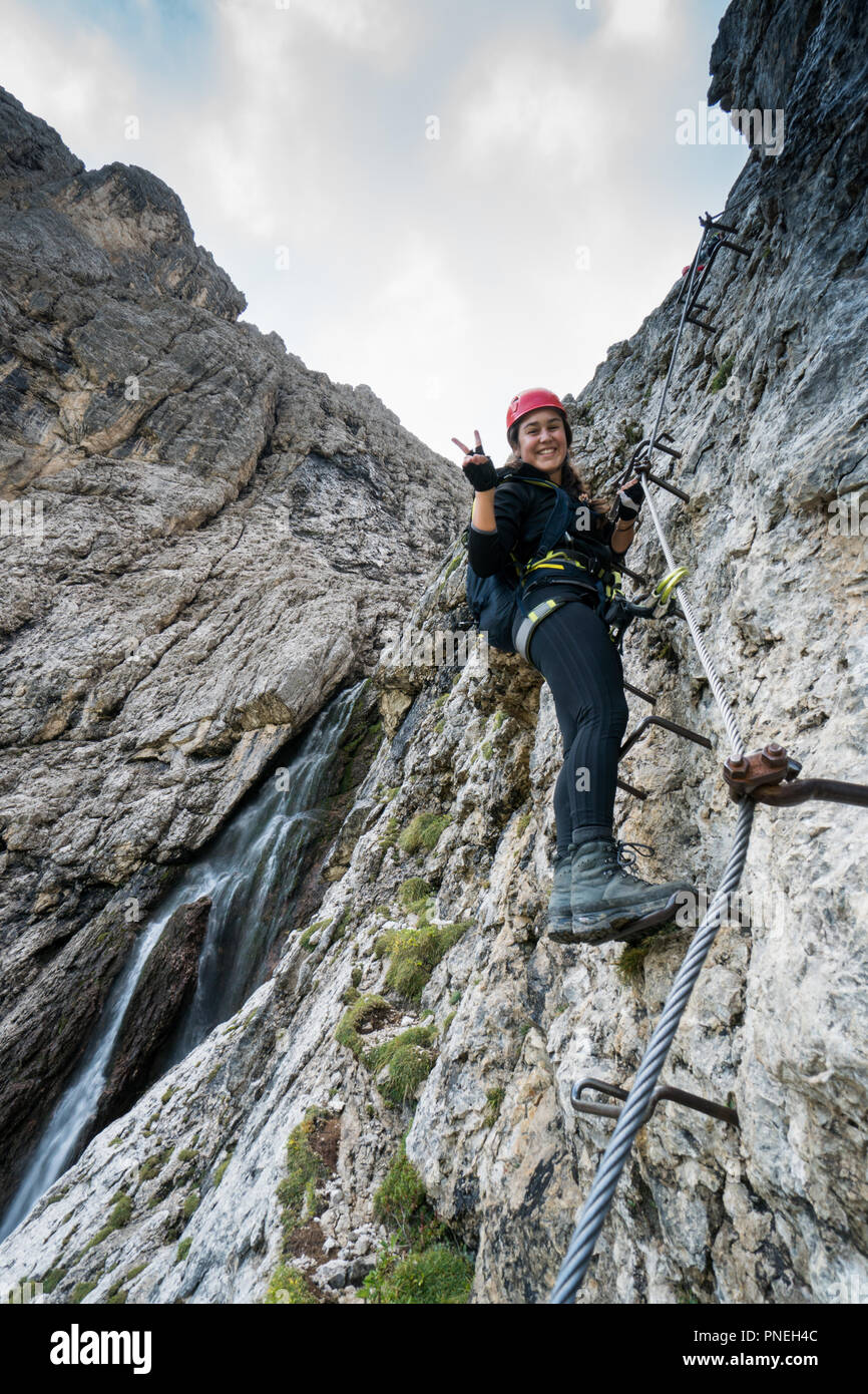 Les jeunes femmes attrayantes d'alpiniste sur une difficile via ferrata dans les Dolomites en Alta Badia dans le Sud Tyrol en Italie faisant un signe de la paix et Banque D'Images