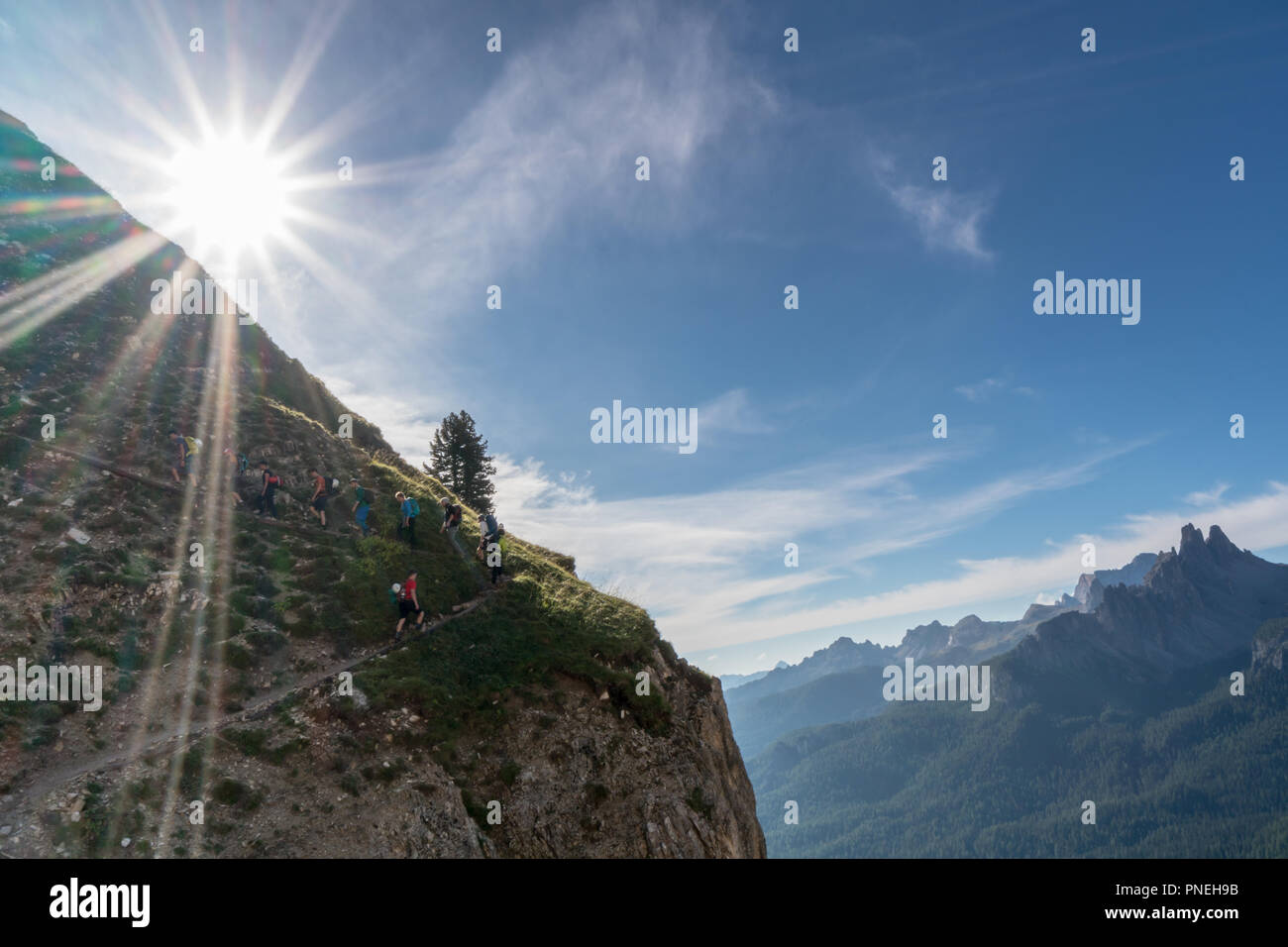 Grand groupe de jeunes randonneurs qui monte un sentier de randonnée escarpé avec le soleil qui brille au-dessus d'eux et vue fantastique sur le paysage de montagne derrière Banque D'Images