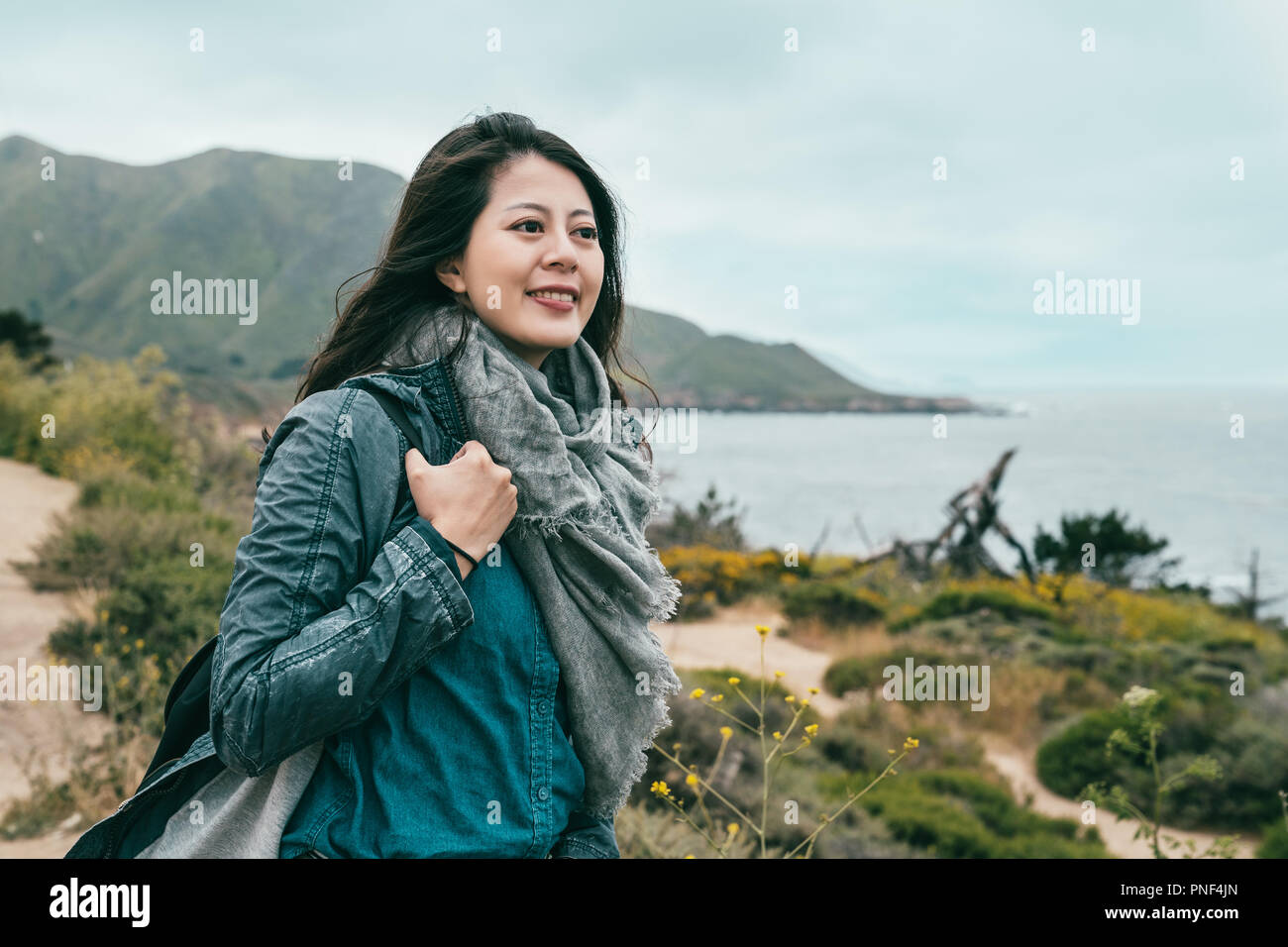 Belle femme à heureux et debout sur la côte près de l'océan brillant et les montagnes. Banque D'Images