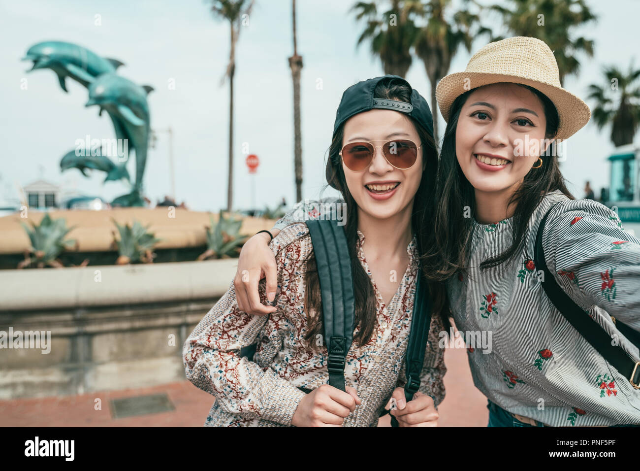 Deux femmes de sourire et de prendre des autoportraits heureusement en face d'une fontaine du dauphin dans une jolie plaza. Banque D'Images