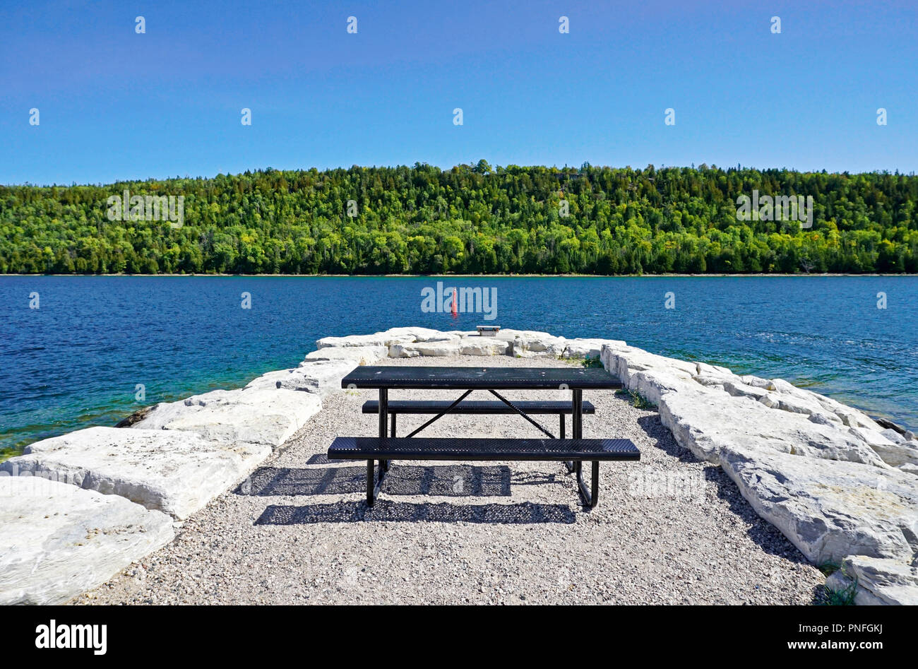 Une forêt luxuriante et d'un bleu profond l'eau et le ciel au-dessus d'une table de pique-nique sur la jetée en pierre à Gore Bay, île Manitoulin, Ontario, Canada Banque D'Images