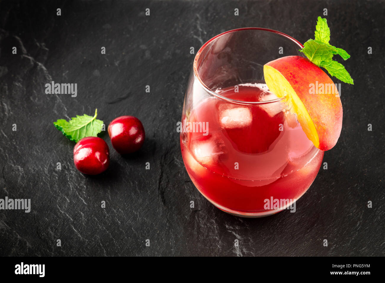 Une photo d'un rouge vibrant verre de cerises, de fruits, et les feuilles de menthe, sur un fond noir avec copie espace Banque D'Images