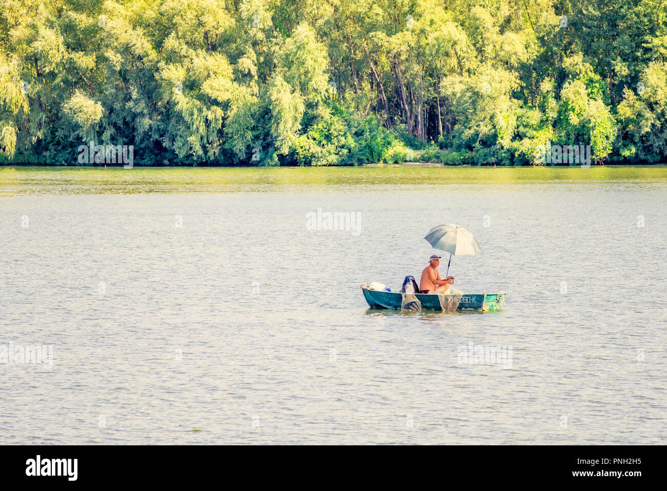 Kiev, Ukraine - 25 août 2015 - Un homme, un pêcheur sur un bateau sur le fleuve Dniepr de Kiev. Il utilise un parapluie pour se protéger de la chaleur somme Banque D'Images