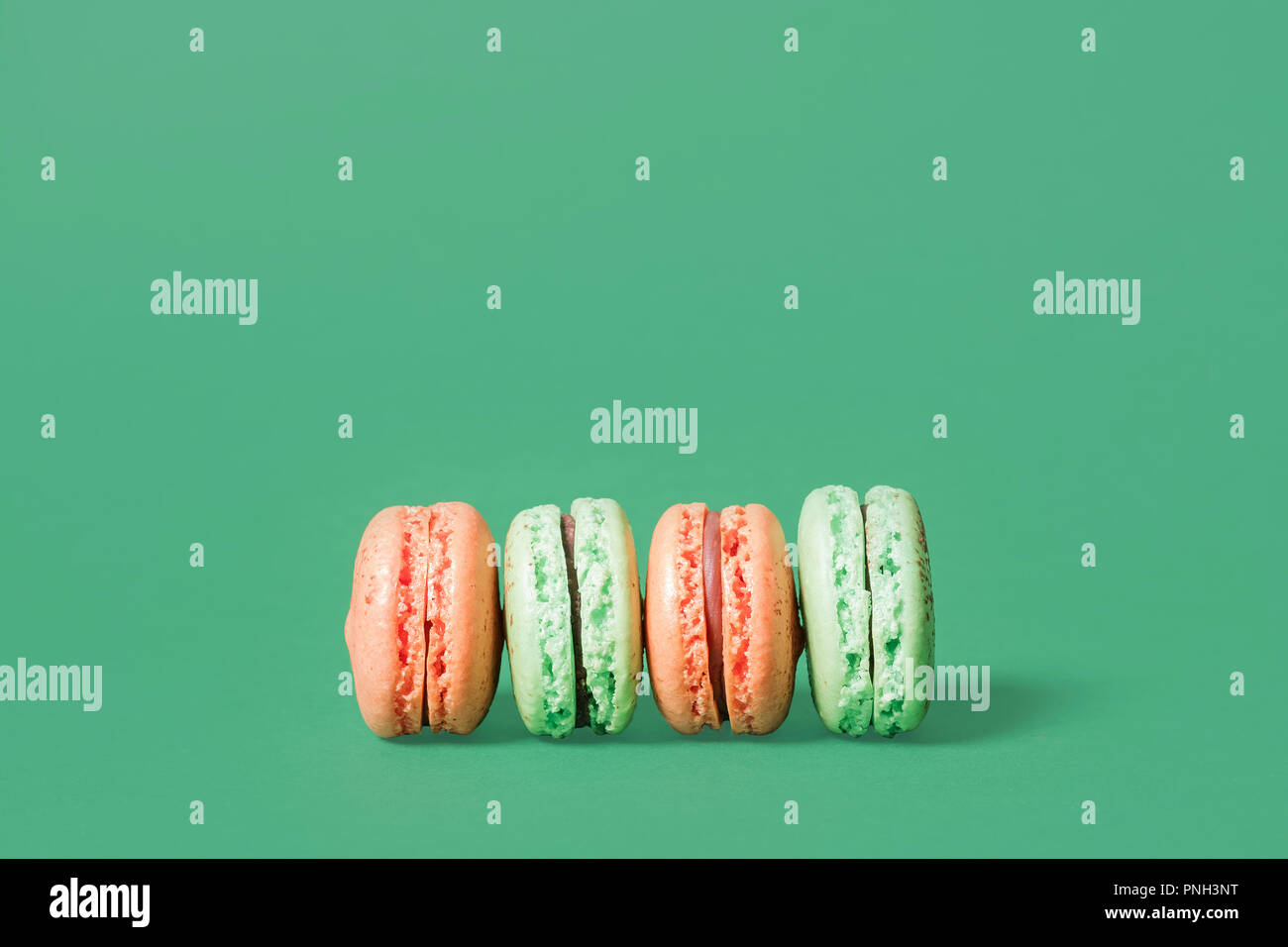 Orange et vert menthe macarons alignés sur le côté sur un fond vert avec espace pour copier et texte Banque D'Images