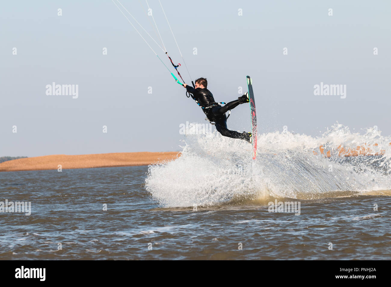 Kiteboarder tirant d'air et d'obtenir des astuces sur un jour d'été parfait avec ciel bleu clair. Strret bardeaux, Suffolk, UK Banque D'Images