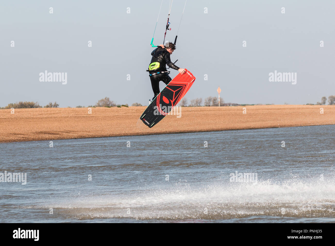 Kiteboarder tirant d'air et d'obtenir des astuces sur un jour d'été parfait avec ciel bleu clair. Strret bardeaux, Suffolk, UK Banque D'Images