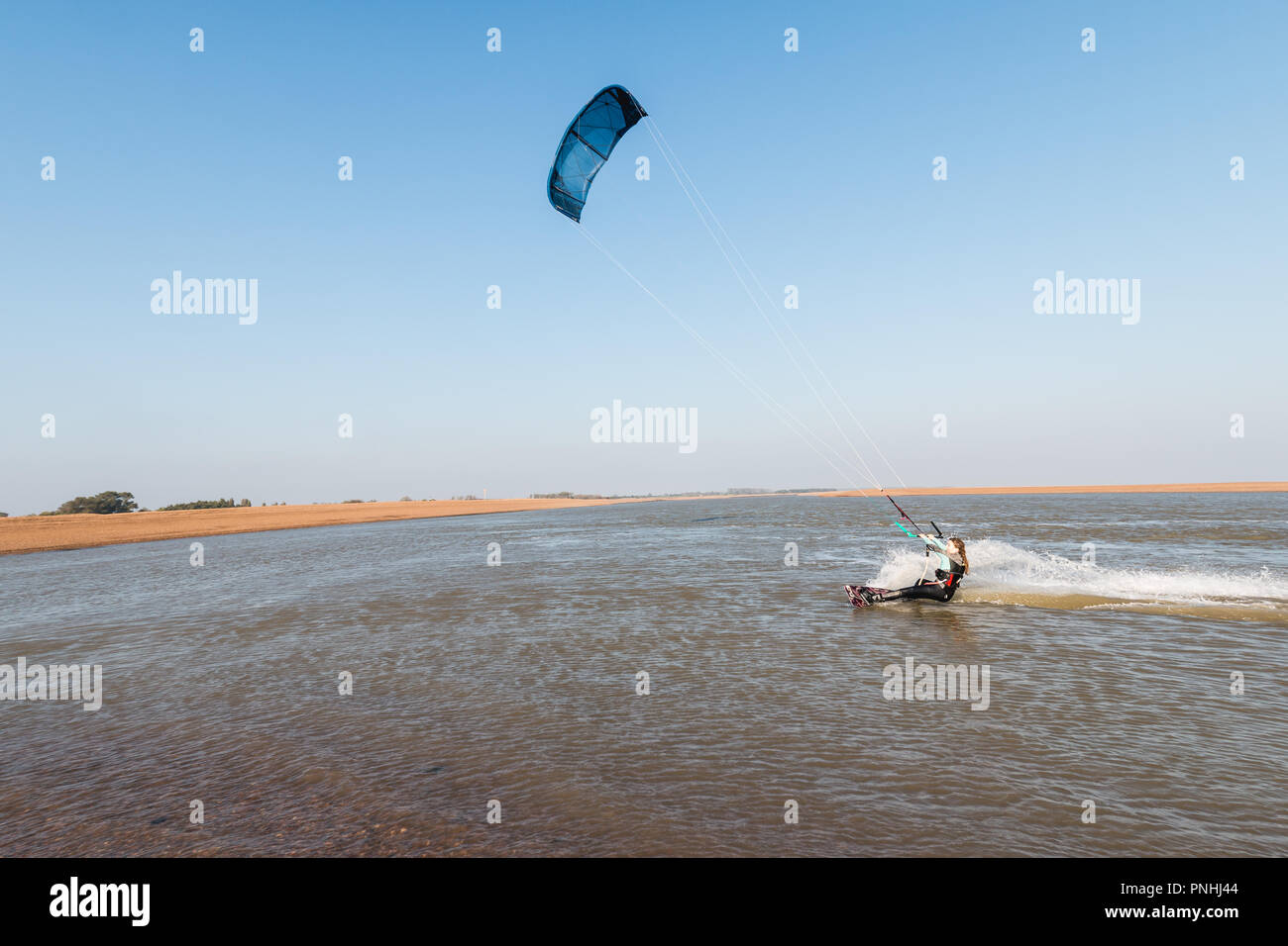 Kiteboarder tirant d'air et d'obtenir des astuces sur un jour d'été parfait avec ciel bleu clair. Strret bardeaux, Suffolk, UK Banque D'Images