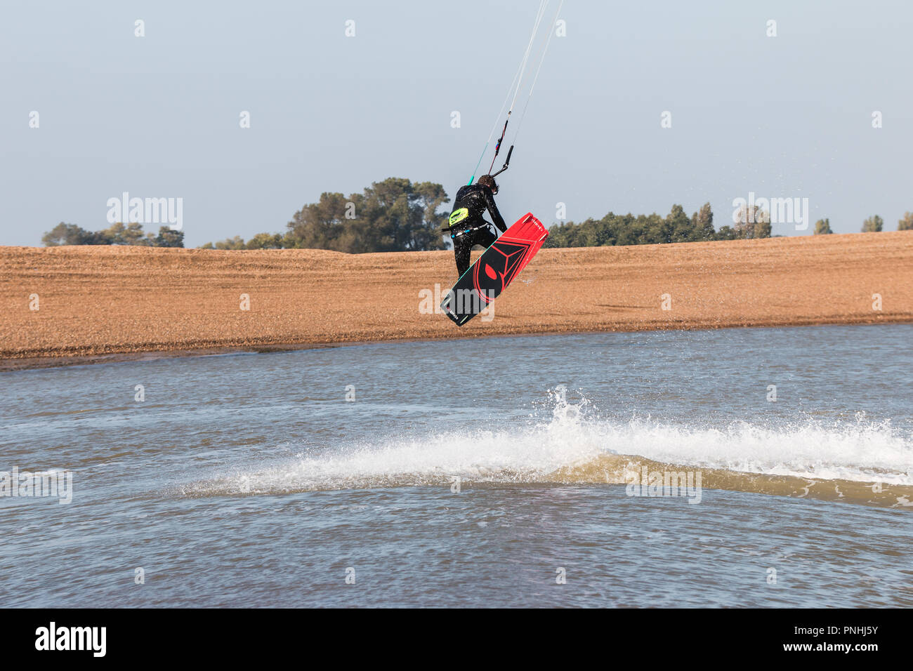 Kiteboarder tirant d'air et d'obtenir des astuces sur un jour d'été parfait avec ciel bleu clair. Strret bardeaux, Suffolk, UK Banque D'Images