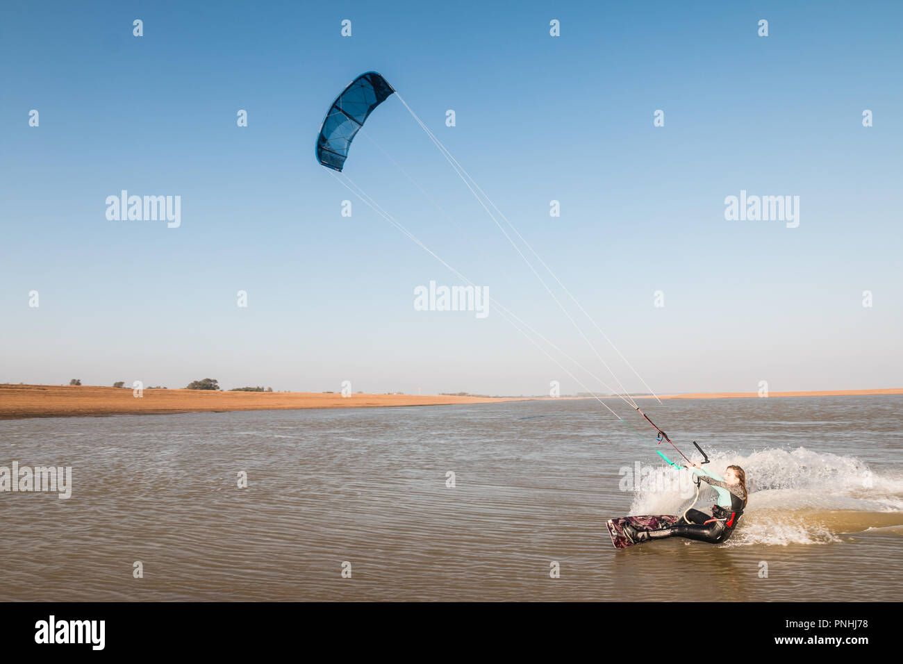Kiteboarder tirant d'air et d'obtenir des astuces sur un jour d'été parfait avec ciel bleu clair. Strret bardeaux, Suffolk, UK Banque D'Images