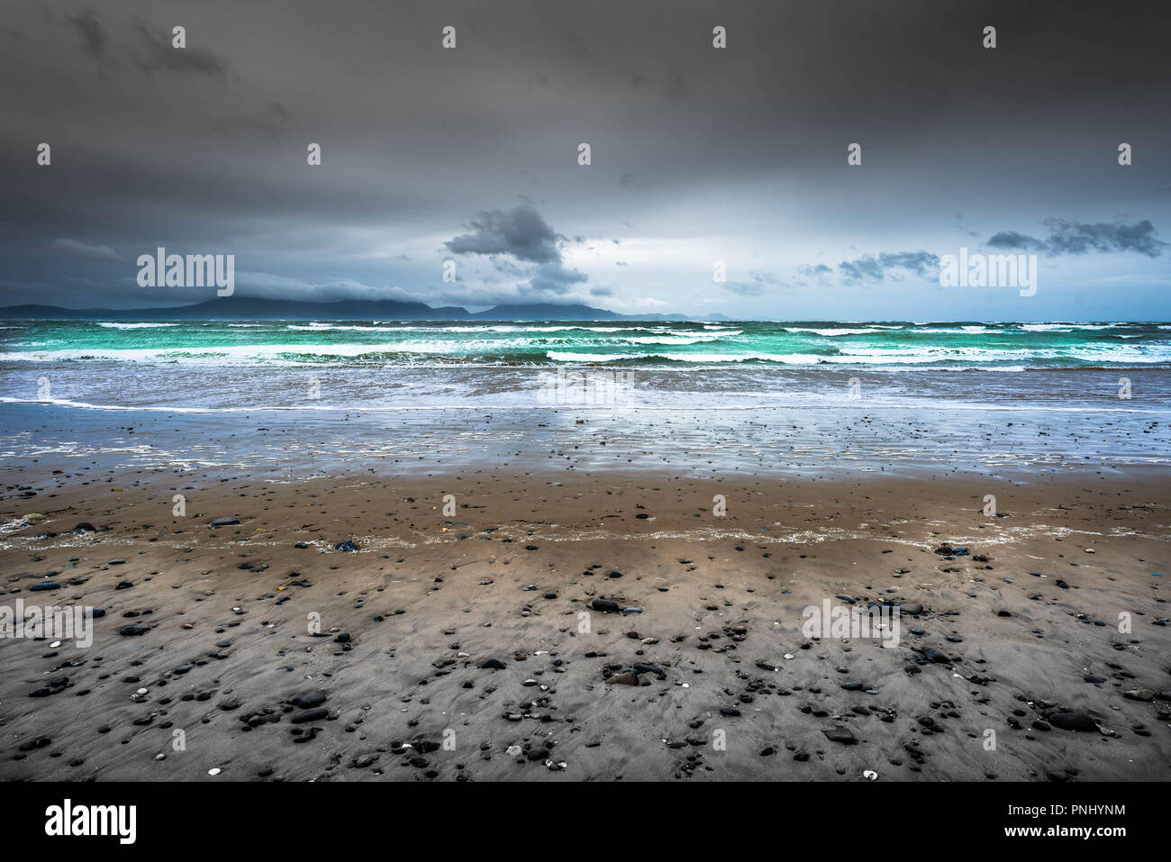 Moody la lumière et ciel sur la plage Llanddwyn Newborough, avec le parc national de Snowdonia au loin., Anglesey, Pays de Galles, Royaume-Uni. Banque D'Images