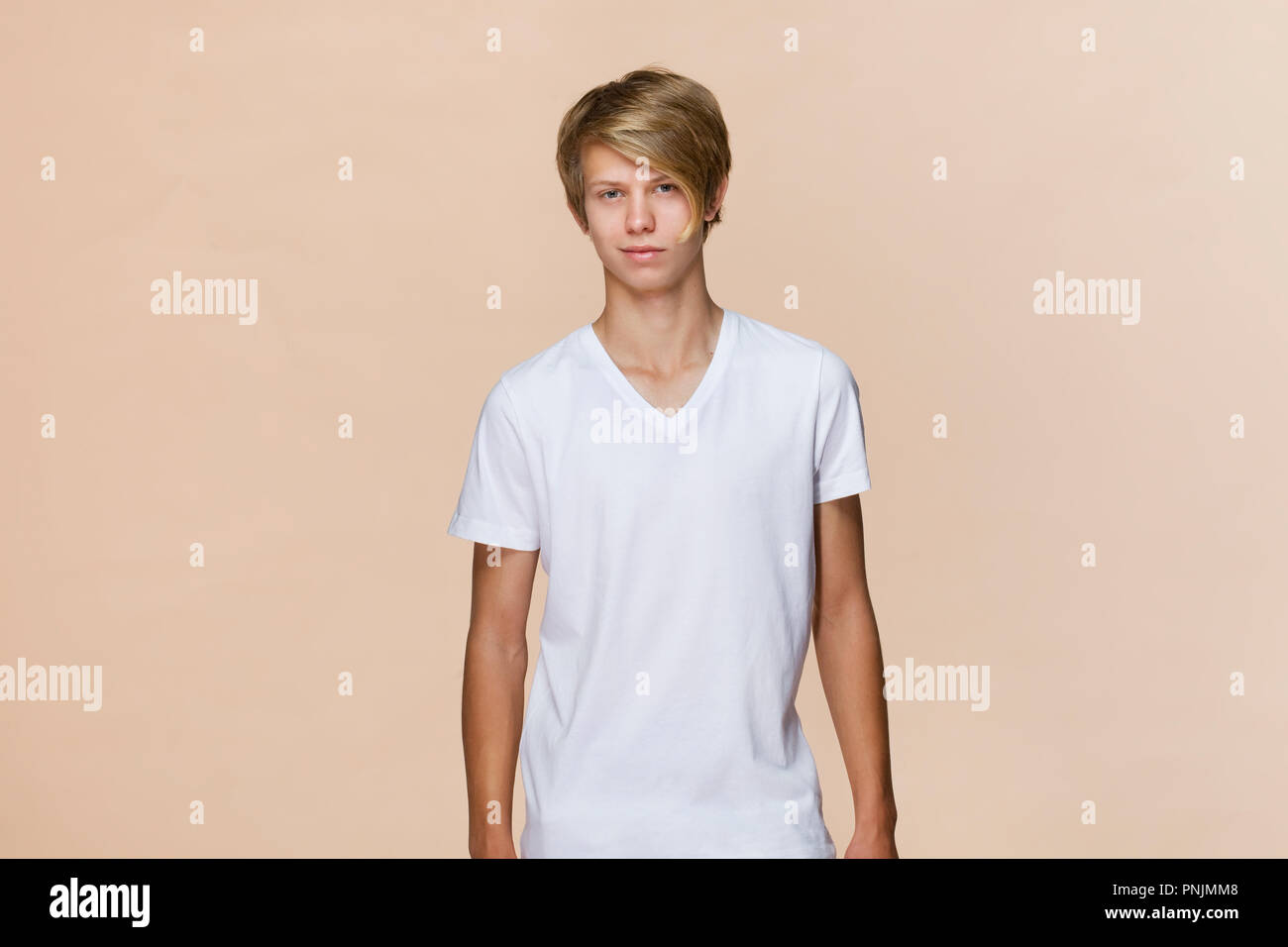 Des hommes souriant avec aspect attrayant, vêtus de T-shirt, posant contre mur blanc marron clair. Homme heureux avec cheveux bun montrant des émotions positives Banque D'Images