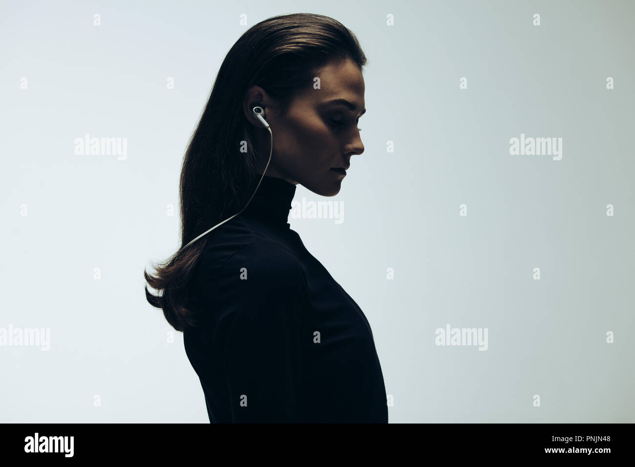 Silhouette de modèle féminin en studio. Side view of young woman wearing earphones sur fond gris. Banque D'Images