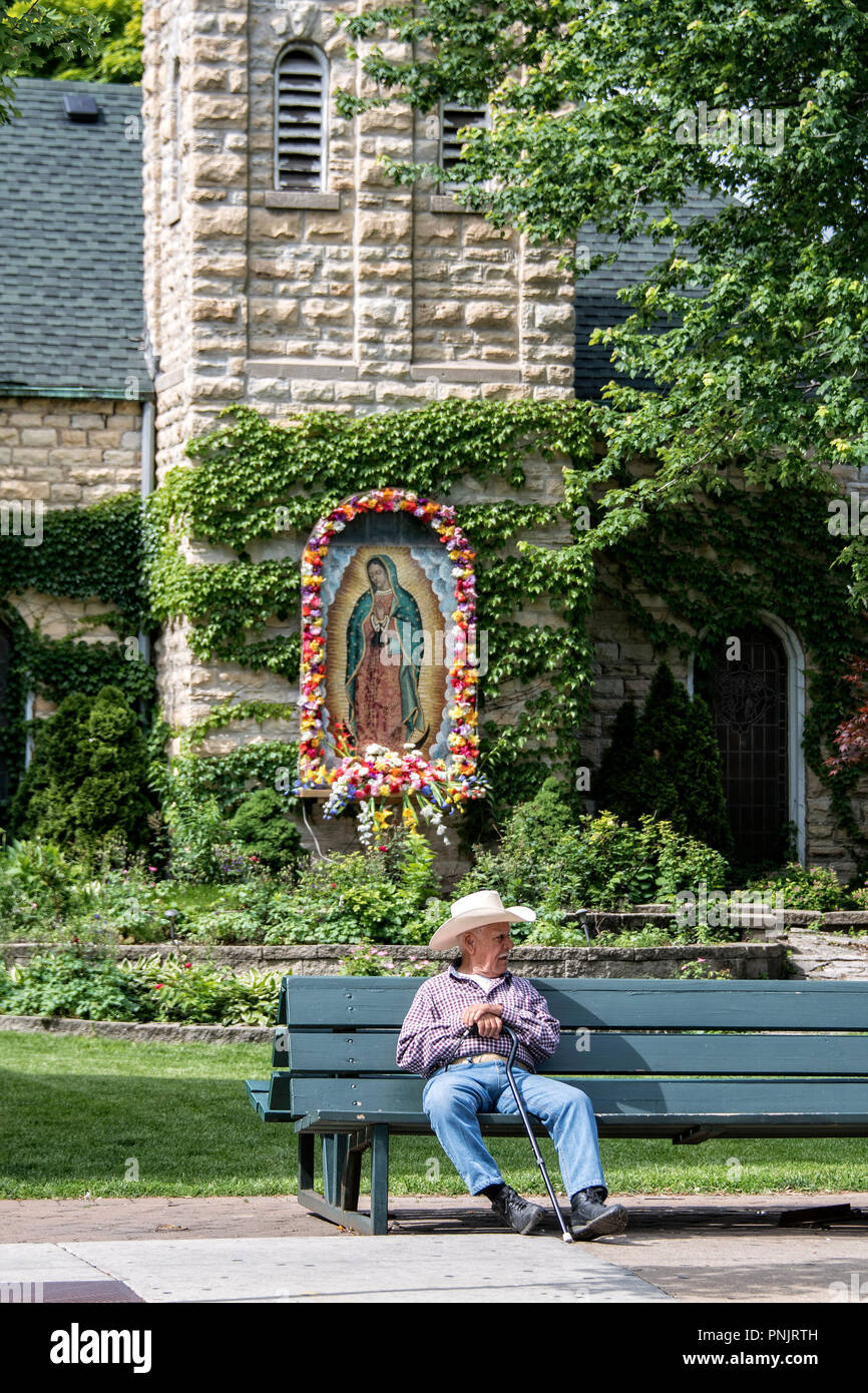 Vieil homme à chapeau de cowboy sur un banc en face d'une image sacrée dans le quartier de Pilsen, quartier historique de la basse côté ouest de Chicago, IL. Banque D'Images