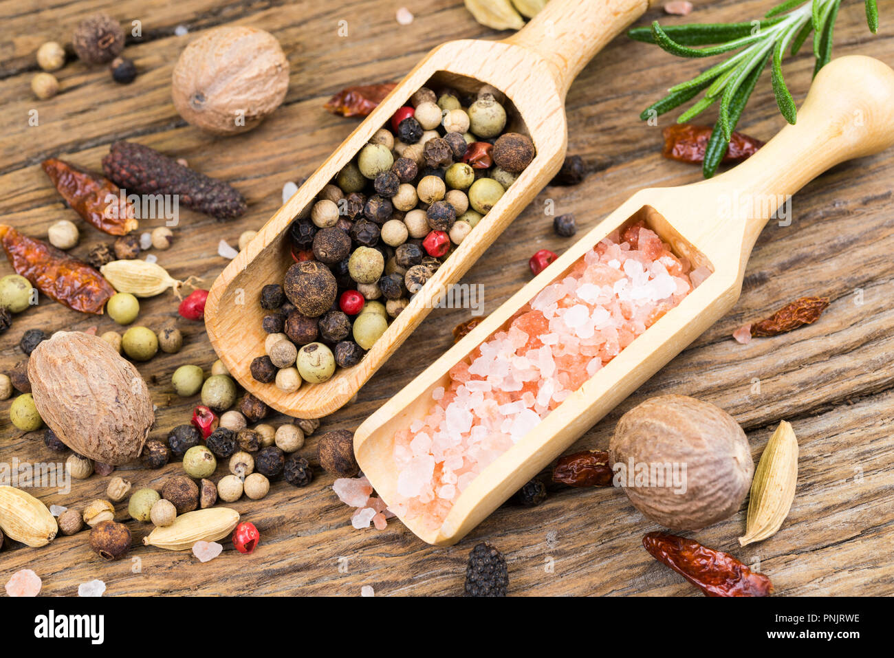 Gros plan du poivre colorés et cristal de couleur rose de sel sur les petites boules à épices en bois sur fond de bois rustique avec un brin de romarin dans le backgroun Banque D'Images