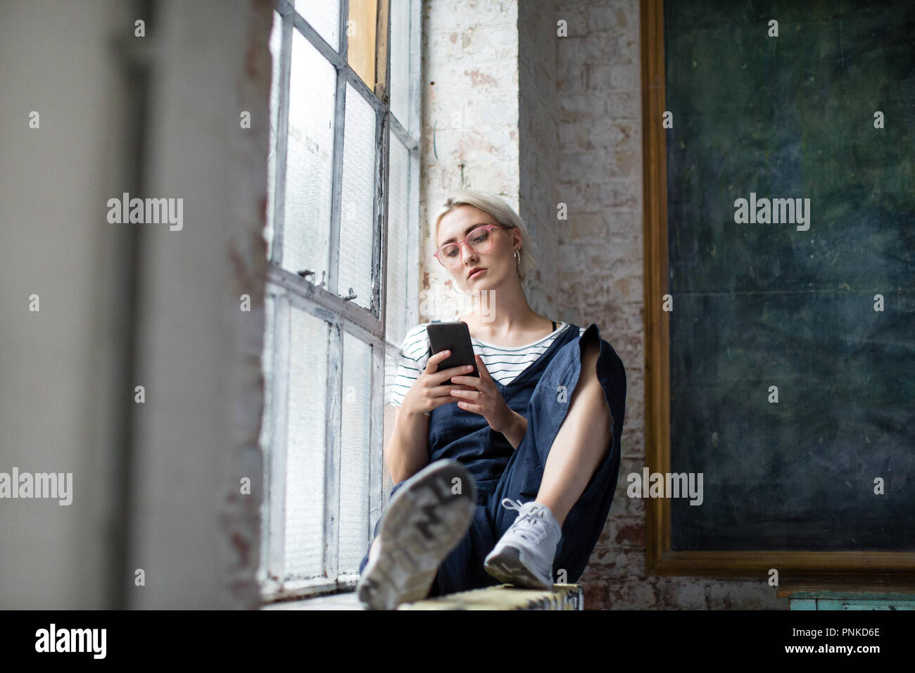 L'utilisation millénaire smartphone par fenêtre dans un loft Banque D'Images