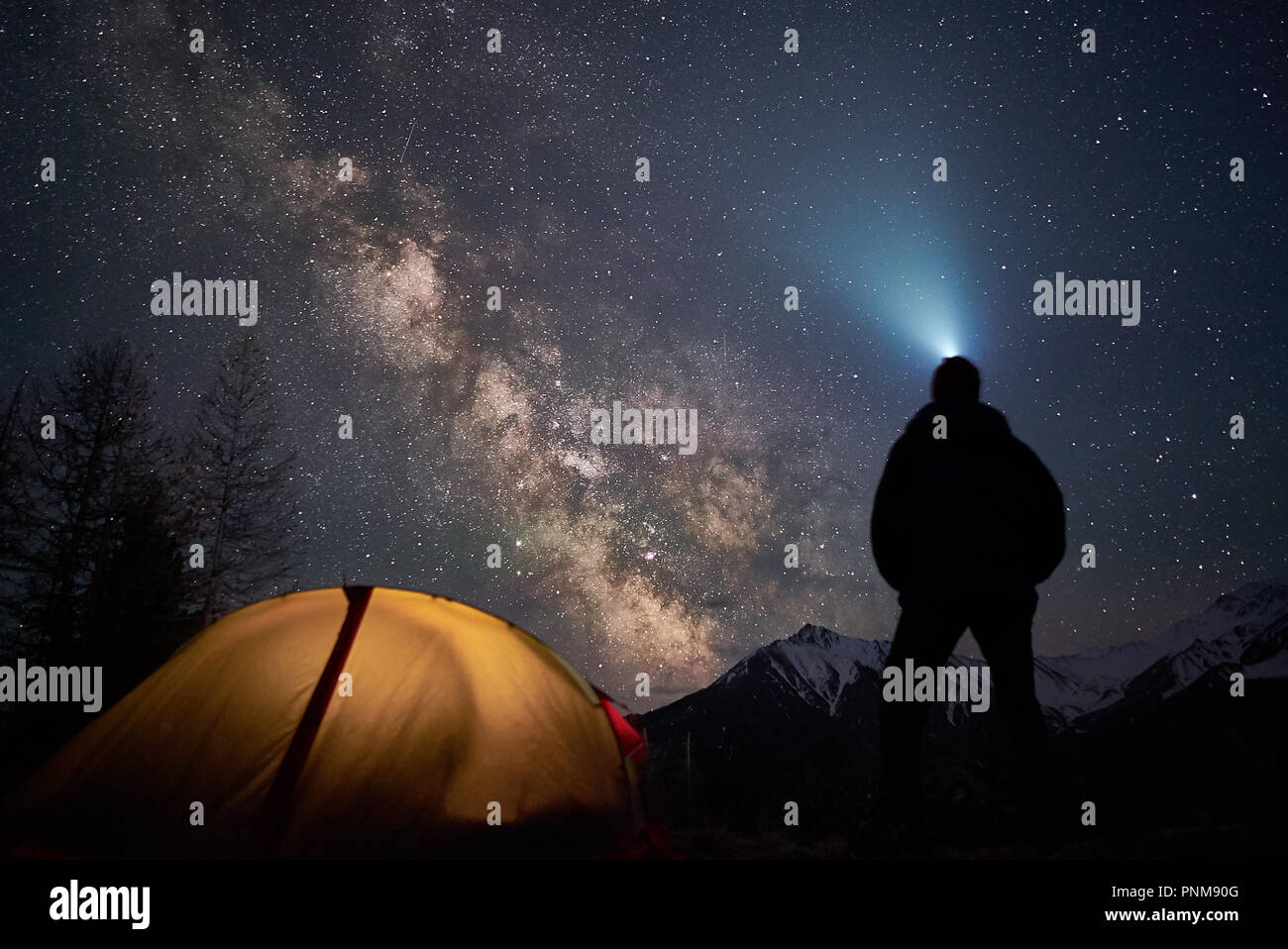 L'homme avec une lampe de poche se trouve près de son camp tente de nuit sous un ciel plein d'étoiles. Banque D'Images