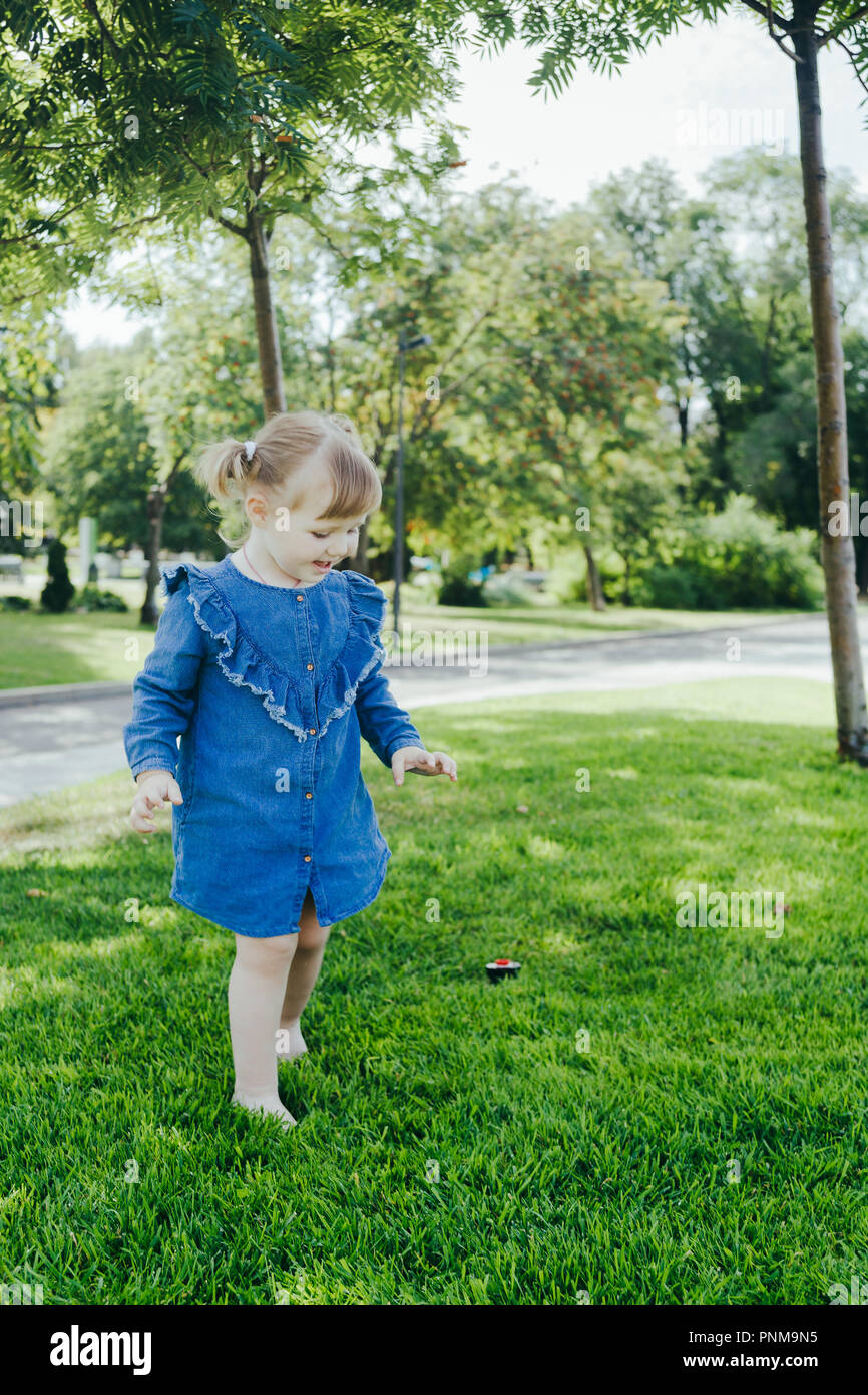 La petite fille en bleu Jean robe pieds nus marche sur une pelouse dans un  parc de la ville dans le centre de Moscou par une chaude journée  ensoleillée Photo Stock -