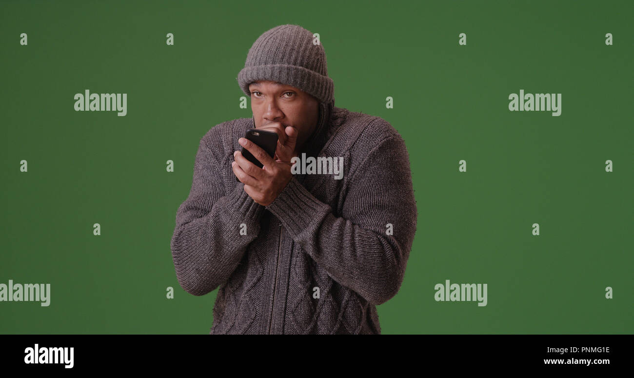 African American man in beanie et sweater texting on téléphone sur un écran vert Banque D'Images