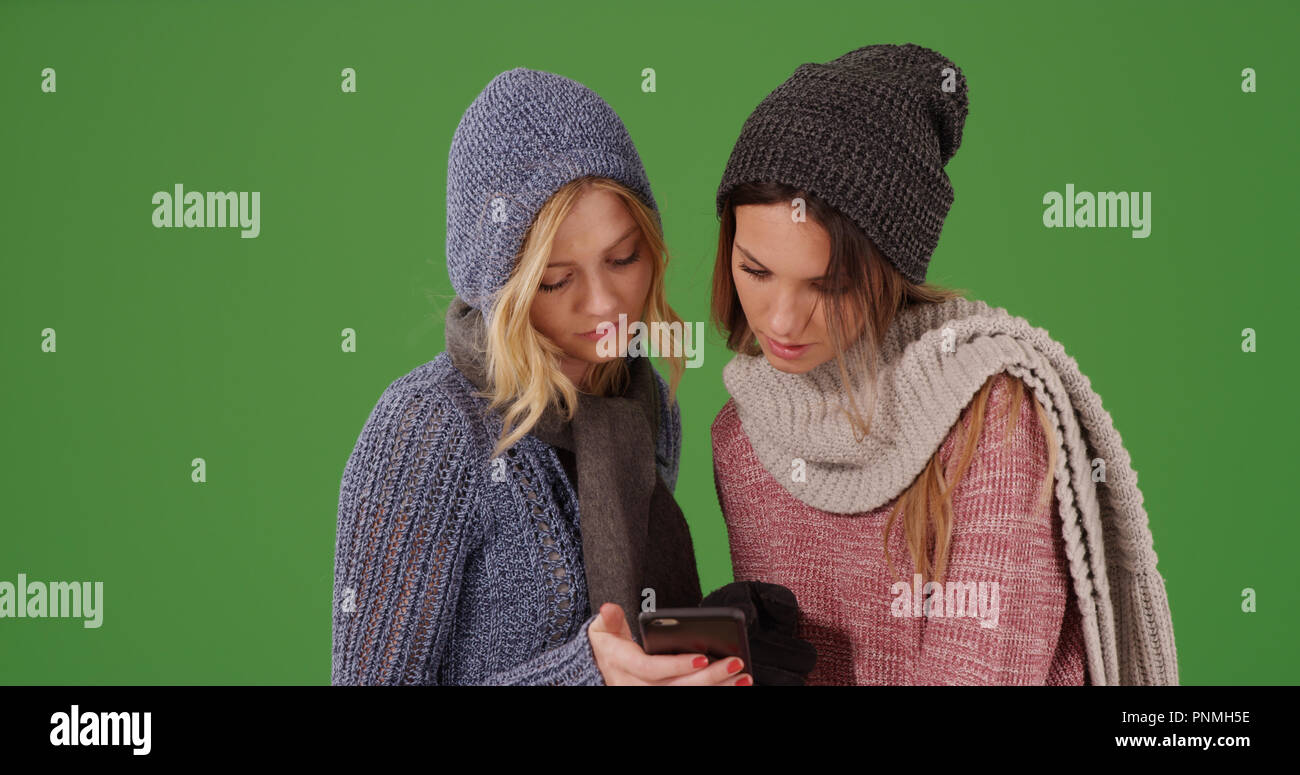 Deux jeunes femmes dans des vêtements d'hiver partager mobile sur un écran vert Banque D'Images