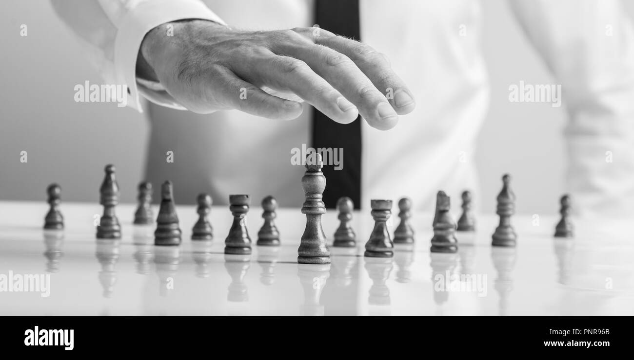 Image Monochrome d'un businessman holding sa main au-dessus de pièces d'échecs en bois avec lit king à l'avant dans une image conceptuelle de business leadership et p Banque D'Images