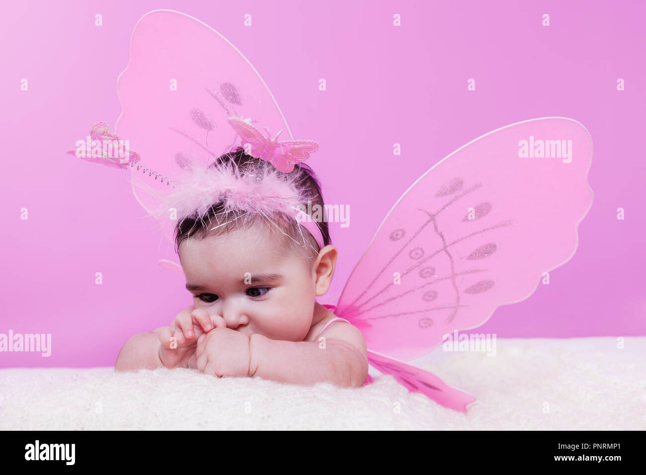 Mignon, joli, heureuse, fille de bébé joufflu curieux au sujet de ses mains, avec les ailes de papillon rose et serre-tête avec des antennes comme les papillons. 4 mois Banque D'Images