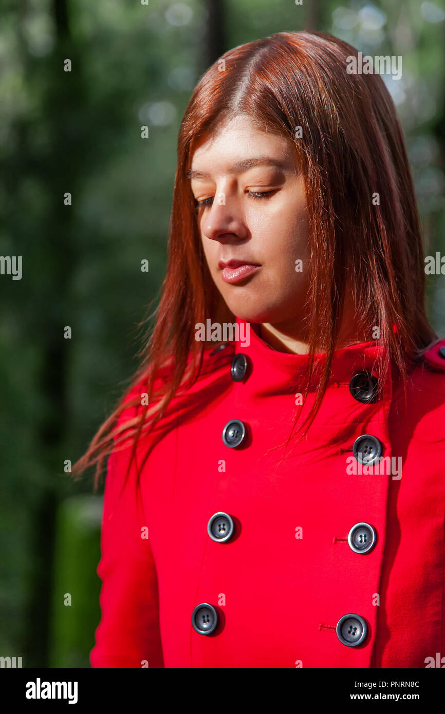 Jeune femme se sentir triste marcher seule sur chemin forestier porter du rouge long manteau ou pardessus. Girl passe la voie sur à pied dans les bois du parc au cours de l'automne, Banque D'Images