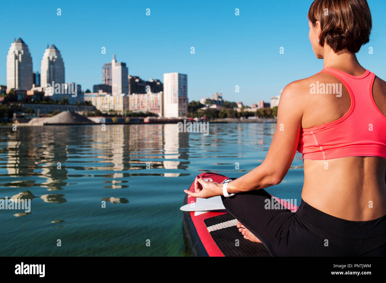 Stand Up Paddle board yoga effectué par belle fille sur la ville, l'arrière-plan lumineux sur l'eau formation de yoga Banque D'Images