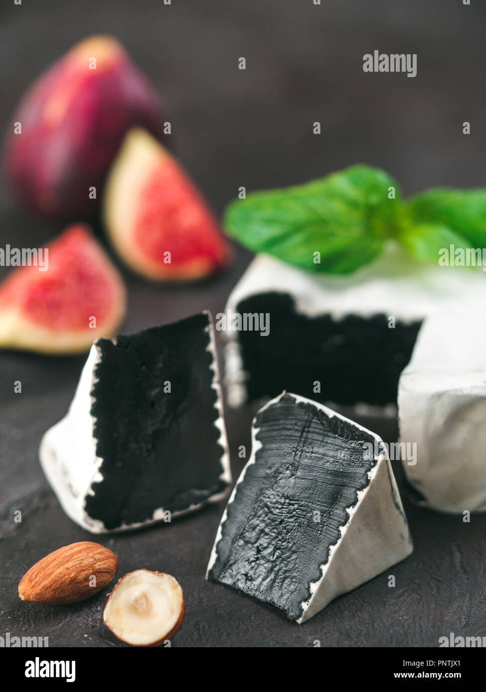 Camembert noir inhabituel avec moisissure blanche.cuisine moderne très tendance, de repas, de l'alimentation.Vue rapprochée du slice noir bio camembert, basilic vert frais, figues, noix sur fond noir.Copy space.Vertical Banque D'Images